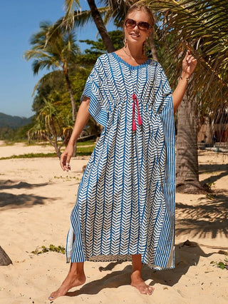 A woman wearing a blue cheap kaftan dress with sun glasses at the beach.