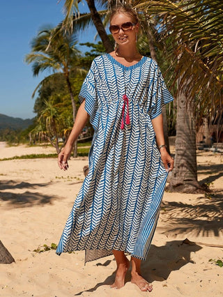 A woman wearing a blue short sleeve kaftan dress with sun glasses at the beach.
