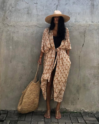 A woman wearing a yellow leaf long kimono cardigan with a bag.